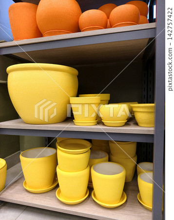 Ceramic flower pots in yellow and red colors with saucers in assorted sizes displayed on shelves in a shopping mall store section 142757422