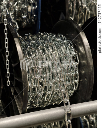 Heavy silver colored steel chain arranged on a spool in a hardware store showcasing robust metal components designed for industrial use and demanding tasks Heavy silver colored steel chain arranged on a spool in a hardware store showcasing robust metal components designed for industrial use and demanding tasks 142757435