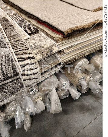 Carpet showroom interior with display racks and neatly wrapped rolled carpets below 142757438