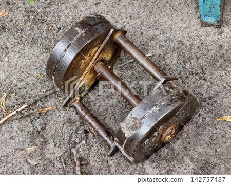Heavy old iron dumbbell lying on the ground of an outdoor sports area for strength training bodybuilding and physical fitness exercise Heavy old iron dumbbell lying on the ground of an outdoor sports area for strength training bodybuilding and physical fitness exercise 142757487