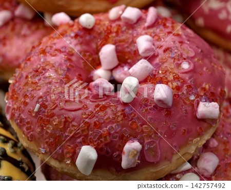 Fresh ring donuts covered with red glaze and white marshmallow pieces displayed in a bakery, showcasing sweet pastries arranged attractively for customers and shoppers Fresh ring donuts covered with red glaze and white marshmallow pieces displayed in a bakery, showcasing sweet pastries arranged attractively for customers and shoppers 142757492