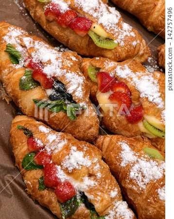 Fresh fruit filled croissants with strawberry kiwi and blueberries displayed in a bakery, highlighting sweet baked pastries finished with powdered sugar for customers Fresh fruit filled croissants with strawberry kiwi and blueberries displayed in a bakery, highlighting sweet baked pastries finished with powdered sugar for customers 142757496
