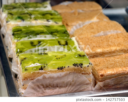 Pastries with green kiwi jelly and pastries decorated with yellow crumbs stand in a confectionery display case, offering a colorful and appealing dessert selection Pastries with green kiwi jelly and pastries decorated with yellow crumbs stand in a confectionery display case, offering a colorful and appealing dessert selection 142757503