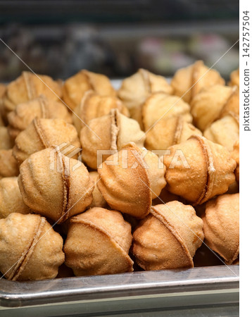 Walnut shaped pastries filled with boiled condensed milk stand in a confectionery display case, offering an appealing dessert selection with a rich sweet filling Walnut shaped pastries filled with boiled condensed milk stand in a confectionery display case, offering an appealing dessert selection with a rich sweet filling 142757504