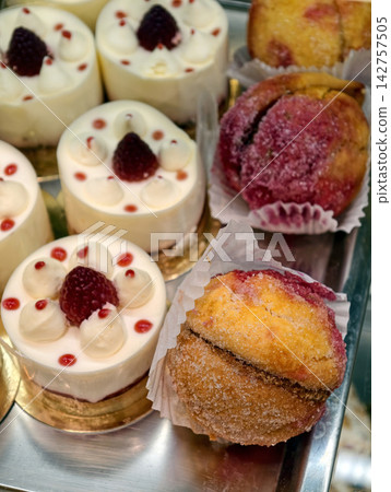 Sugar covered peach shaped pastries and white cream pastries with a real raspberry in the center form an attractive and varied dessert display in a confectionery shop 142757505