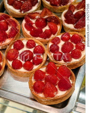 Round tartlets decorated with fresh red strawberries stand on a confectionery display case, creating an elegant presentation of sweet pastries with natural fruit 142757506