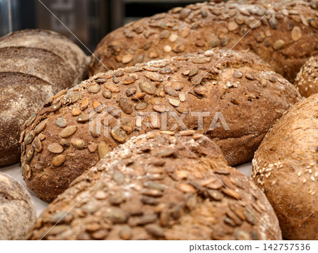 Dark rye bread covered with pumpkin seeds displayed in a bakery, showcasing a fresh baked loaf with a textured crust and a generous seed topping Dark rye bread covered with pumpkin seeds displayed in a bakery, showcasing a fresh baked loaf with a textured crust and a generous seed topping 142757536