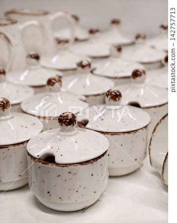 Ceramic sauce bowls or sugar containers in light tones lined up in retail display highlighting simple tableware collection intended for serving and storage in modern kitchen settings Ceramic sauce bowls or sugar containers in light tones lined up in retail display highlighting simple tableware collection intended for serving and storage in modern kitchen settings 142757713