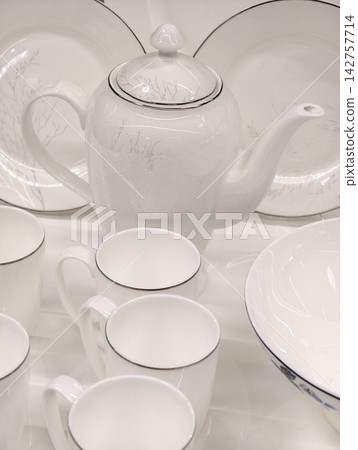 White porcelain cups teapot and plates in elegant design displayed on retail shelf forming premium kitchenware set ready for sale and appealing to customers in store environment White porcelain cups teapot and plates in elegant design displayed on retail shelf forming premium kitchenware set ready for sale and appealing to customers in store environment 142757714