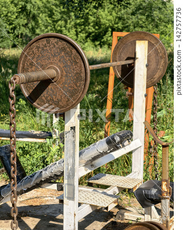 Barbell with metal weight plates resting on an incline bench at an outdoor training area for bodybuilding workouts and upper body strength development Barbell with metal weight plates resting on an incline bench at an outdoor training area for bodybuilding workouts and upper body strength development 142757736