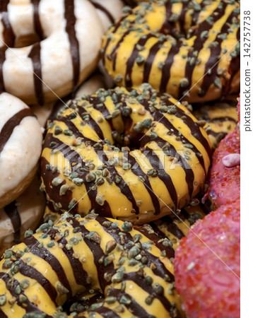Sweet ring donuts covered with yellow glaze and topped with chocolate stripes and seeds displayed in a bakery, showcasing fresh baked products for shoppers Sweet ring donuts covered with yellow glaze and topped with chocolate stripes and seeds displayed in a bakery, showcasing fresh baked products for shoppers 142757738