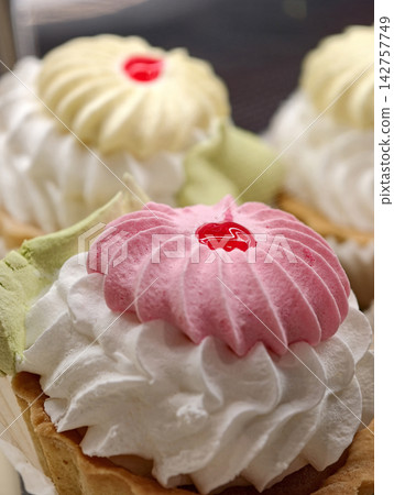 Cream and marshmallow pastries in white paper wrappers displayed in a pastry shop showcase, offering an inviting selection of light sweet desserts with a delicate appearance Cream and marshmallow pastries in white paper wrappers displayed in a pastry shop showcase, offering an inviting selection of light sweet desserts with a delicate appearance 142757749