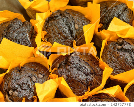 Dark cupcakes in yellow paper wrappers displayed in a bakery, showcasing fresh baked pastries arranged attractively as part of the sweet selection for customers Dark cupcakes in yellow paper wrappers displayed in a bakery, showcasing fresh baked pastries arranged attractively as part of the sweet selection for customers 142757778