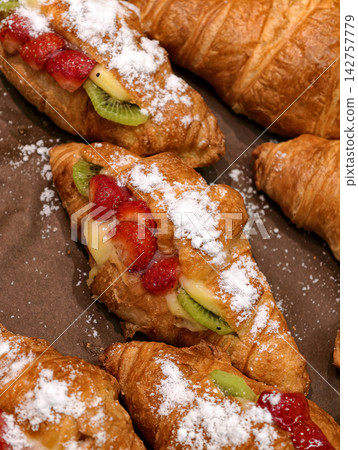 Fresh croissants filled with strawberry and kiwi pieces displayed in a bakery, featuring sweet baked pastries dusted with powdered sugar and presented for customers Fresh croissants filled with strawberry and kiwi pieces displayed in a bakery, featuring sweet baked pastries dusted with powdered sugar and presented for customers 142757779