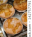 Round apple pies placed in foil dishes are arranged in a confectionery display, creating a neat presentation of sweet pastries with a delicious apple filling 142757791