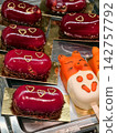 Red oval pastries covered with glaze and decorated with painted hearts are arranged in a confectionery display case, creating an attractive sweet dessert presentation 142757792