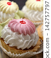 Light cream pastries with marshmallow in white paper wrapping arranged in a pastry shop showcase, highlighting an appetizing display of soft airy desserts with delicate appearance 142757797