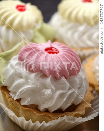 Light cream pastries with marshmallow in white paper wrapping arranged in a pastry shop showcase, highlighting an appetizing display of soft airy desserts with delicate appearance Light cream pastries with marshmallow in white paper wrapping arranged in a pastry shop showcase, highlighting an appetizing display of soft airy desserts with delicate appearance 142757797
