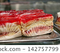 Cream filled puff pastries with a red jelly topping displayed in a pastry shop showcase, creating an appealing presentation of a sweet layered dessert with glossy finish 142757799