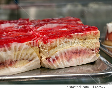 Cream filled puff pastries with a red jelly topping displayed in a pastry shop showcase, creating an appealing presentation of a sweet layered dessert with glossy finish Cream filled puff pastries with a red jelly topping displayed in a pastry shop showcase, creating an appealing presentation of a sweet layered dessert with glossy finish 142757799