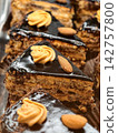 Dark chocolate covered cake slices with almond nuts arranged on a pastry shop display, highlighting an attractive sweet dessert with a rich topping and crunchy texture 142757800