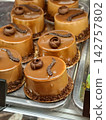 Brown cylindrical pastries covered with grated chocolate displayed in a pastry shop showcase, presenting an appetizing sweet dessert with a rich chocolate topping and elegant shape 142757802
