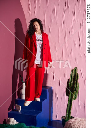 Fashionable woman in red pauses amidst textured wall background Fashionable woman in red pauses amidst textured wall background 142757878