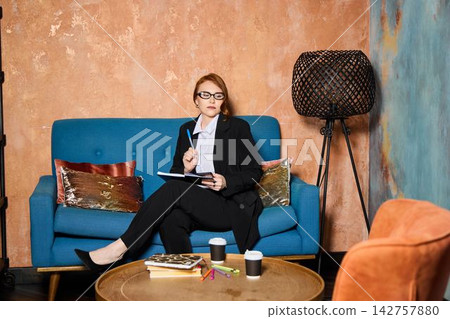 Seated female author drafts manuscript with coffee nearby and glasses Seated female author drafts manuscript with coffee nearby and glasses 142757880