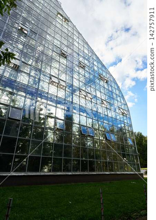 Facade of glass office building with grid of panes and metal frames reflecting blue sky and clouds from angled perspective showcasing modern architecture and glassy exterior Facade of glass office building with grid of panes and metal frames reflecting blue sky and clouds from angled perspective showcasing modern architecture and glassy exterior 142757911