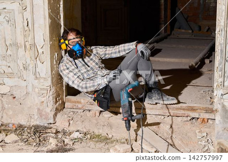Man in safety gear relaxes on dusty windowsill during construction 142757997