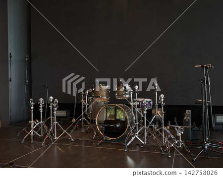 Stage drum kit setup with multiple drums cymbals and microphones on stands under concert lighting and dark backdrop Stage drum kit setup with multiple drums cymbals and microphones on stands under concert lighting and dark backdrop 142758026