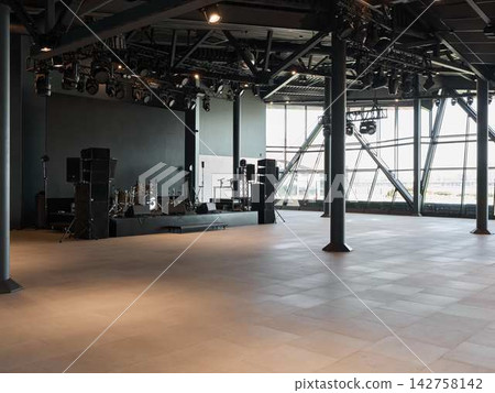Indoor concert hall stage with extensive lighting rig overhead, metal truss framework, and array of instruments including drums, guitars, bass, and amplifiers prepared for live performance Indoor concert hall stage with extensive lighting rig overhead, metal truss framework, and array of instruments including drums, guitars, bass, and amplifiers prepared for live performance 142758142