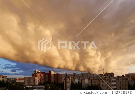 Urban skyline and apartment rooftops beneath dramatic orange storm clouds over city street view at dusk, with glowing light and hints of blue sky behind moving weather fronts Urban skyline and apartment rooftops beneath dramatic orange storm clouds over city street view at dusk, with glowing light and hints of blue sky behind moving weather fronts 142758178