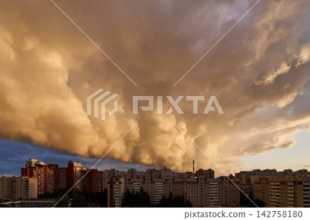 Sunset urban skyline with dense apartment blocks beneath dramatic orange clouds, warm street-level glow over downtown city streets at dusk 142758180