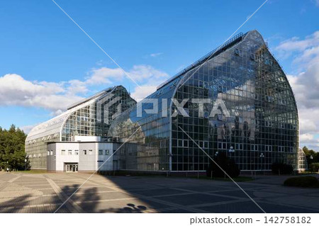 Glass conservatory buildings with clear blue sky, sunlit reflective facades, and modern geometric architecture in spacious outdoor complex Glass conservatory buildings with clear blue sky, sunlit reflective facades, and modern geometric architecture in spacious outdoor complex 142758182