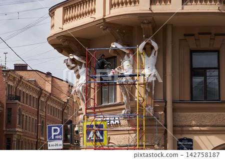 Ornate historic building facade restoration with worker on scaffold applying plaster to sculpted stonework, columns, balustrade, and cornice in daytime street scene Ornate historic building facade restoration with worker on scaffold applying plaster to sculpted stonework, columns, balustrade, and cornice in daytime street scene 142758187