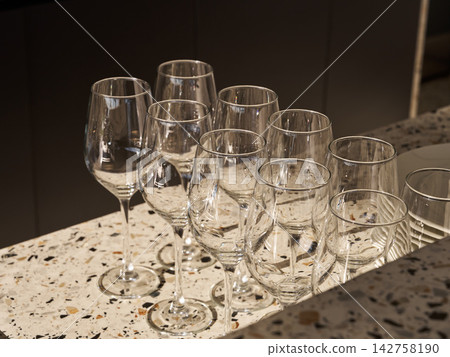 Row of crystal wine glasses on speckled terrazzo table under warm ambient light, elegant glassware centerpiece for celebration toast and party atmosphere Row of crystal wine glasses on speckled terrazzo table under warm ambient light, elegant glassware centerpiece for celebration toast and party atmosphere 142758190