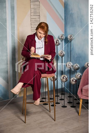Redhead white scriptwriter in burgundy suit jotting notes Redhead white scriptwriter in burgundy suit jotting notes 142758262