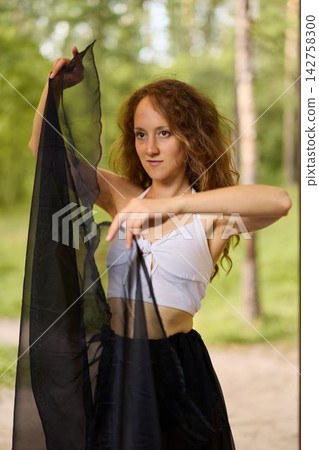Redhaired woman gazes thoughtfully while holding delicate chiffon fabric 142758300