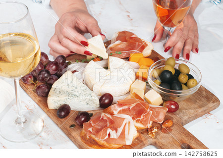 Sharing a cheese board with grapes, meats, and drinks during a gathering at home Sharing a cheese board with grapes, meats, and drinks during a gathering at home 142758625