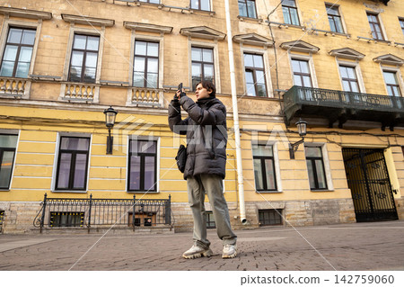 Young man taking photo with smartphone on old city street. Tourist photographing historic architecture with phone. Travel and urban exploration concept. Young man taking photo with smartphone on old city street. Tourist photographing historic architecture with phone. Travel and urban exploration concept. 142759060