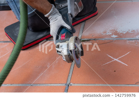 Worker cutting terracotta tiles with angle grinder during floor renovation Worker cutting terracotta tiles with angle grinder during floor renovation 142759976