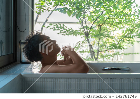 A 40-year-old man's relaxing time enjoying a bath with his eyes closed in a sunlit bathroom. A 40-year-old man's relaxing time enjoying a bath with his eyes closed in a sunlit bathroom. 142761749
