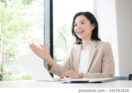 一位五十多歲的女性面帶微笑地與客戶面對面諮詢;一位女商人正在辦公室裡進行解釋和提出建議;溝通。 一位五十多歲的女性面帶微笑地與客戶面對面諮詢;一位女商人正在辦公室裡進行解釋和提出建議;溝通。 142761828