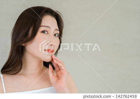 一位四五十歲的女性將手放在下顎線上。這幅畫面展現了抗老護理和美麗肌膚。 142762459
