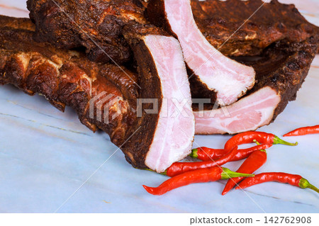 Barbecue pork ribs, red chili peppers on marble table in home kitchen Barbecue pork ribs, red chili peppers on marble table in home kitchen 142762908