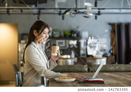 A young woman working while eating breakfast at a cafe. A young woman working while eating breakfast at a cafe. 142763395