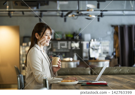 A young woman working while eating breakfast at a cafe. A young woman working while eating breakfast at a cafe. 142763399