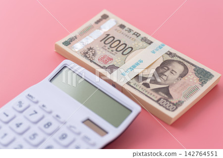 一疊100萬日元鈔票和一個白色計算器，背景是粉紅色的。 142764551