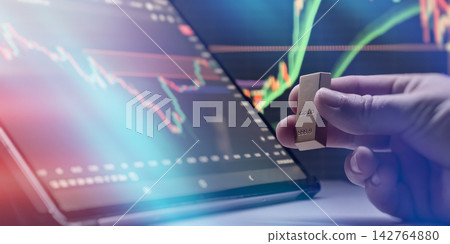 Digital gold commodity trading. Hand holding a gold bullion bar in front of a computer screen with financial market charts Digital gold commodity trading. Hand holding a gold bullion bar in front of a computer screen with financial market charts 142764880